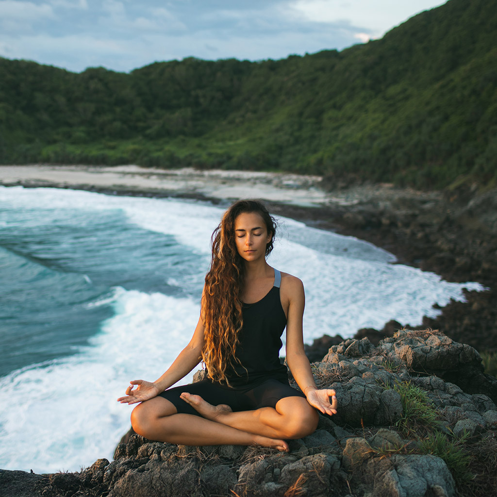 Mujer meditando en postura de loto frente al mar.